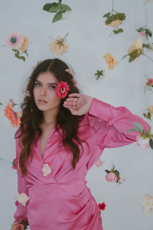 Young Brunette in a Pink Dress Posing among Flowers in Studio 