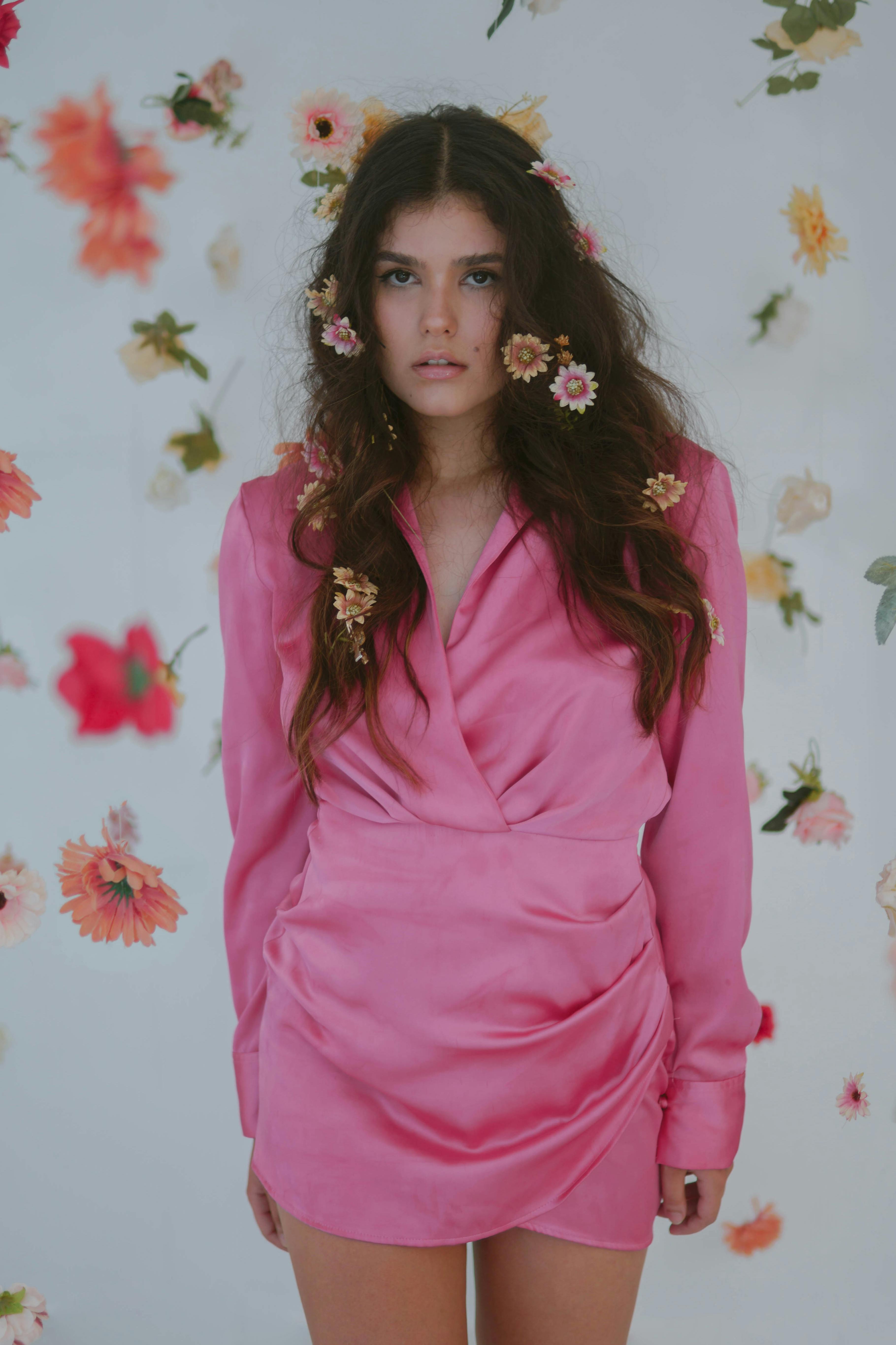 Stylish portrait of brunette woman in pink dress surrounded by floating flowers.