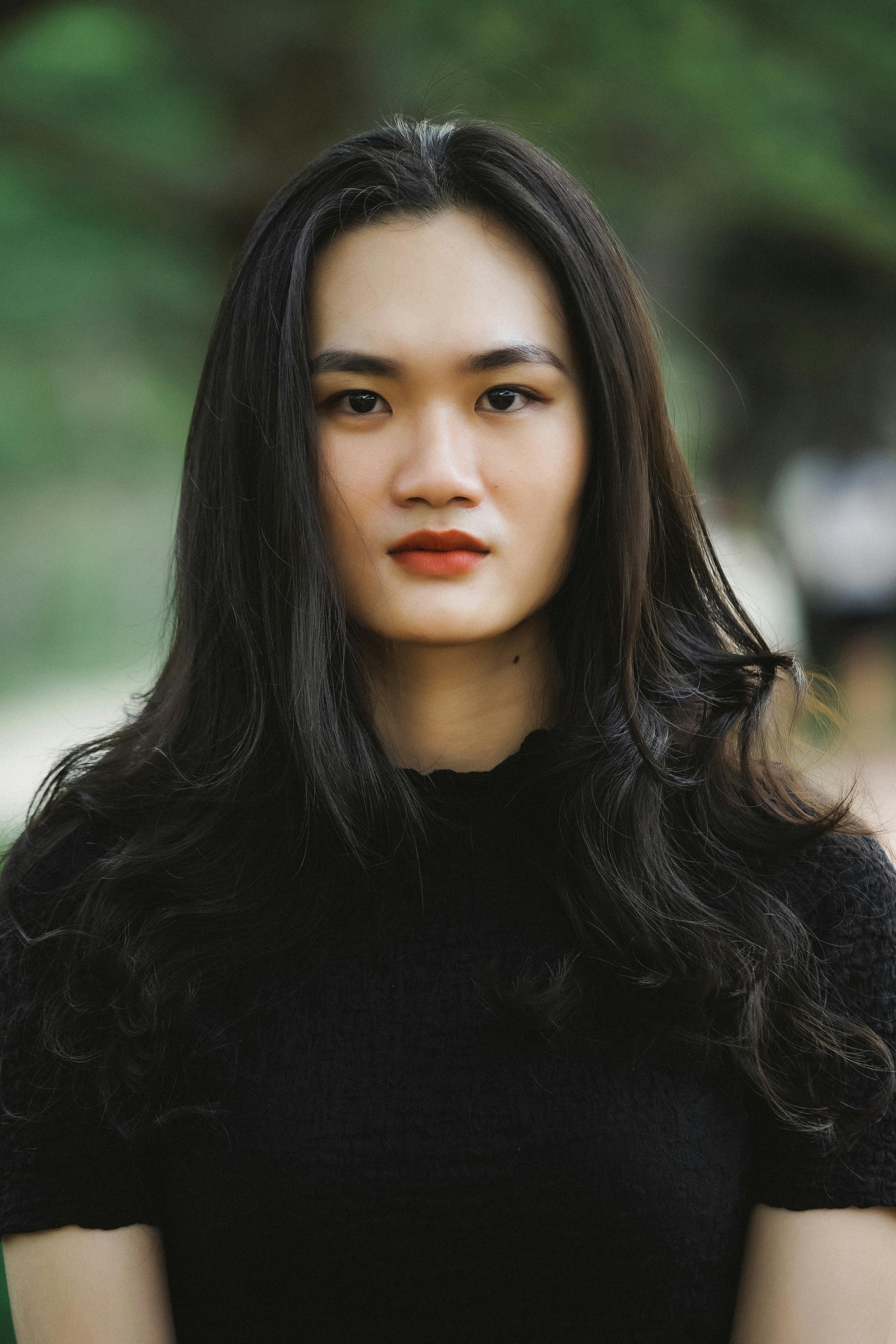 Striking portrait of a young woman with long hair in a natural outdoor setting.