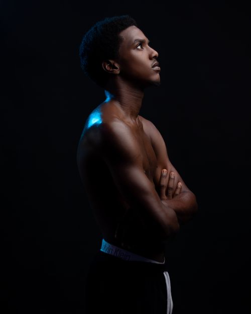 Free Portrait of a young, shirtless man in a studio setting with a dramatic light against a black background. Stock Photo