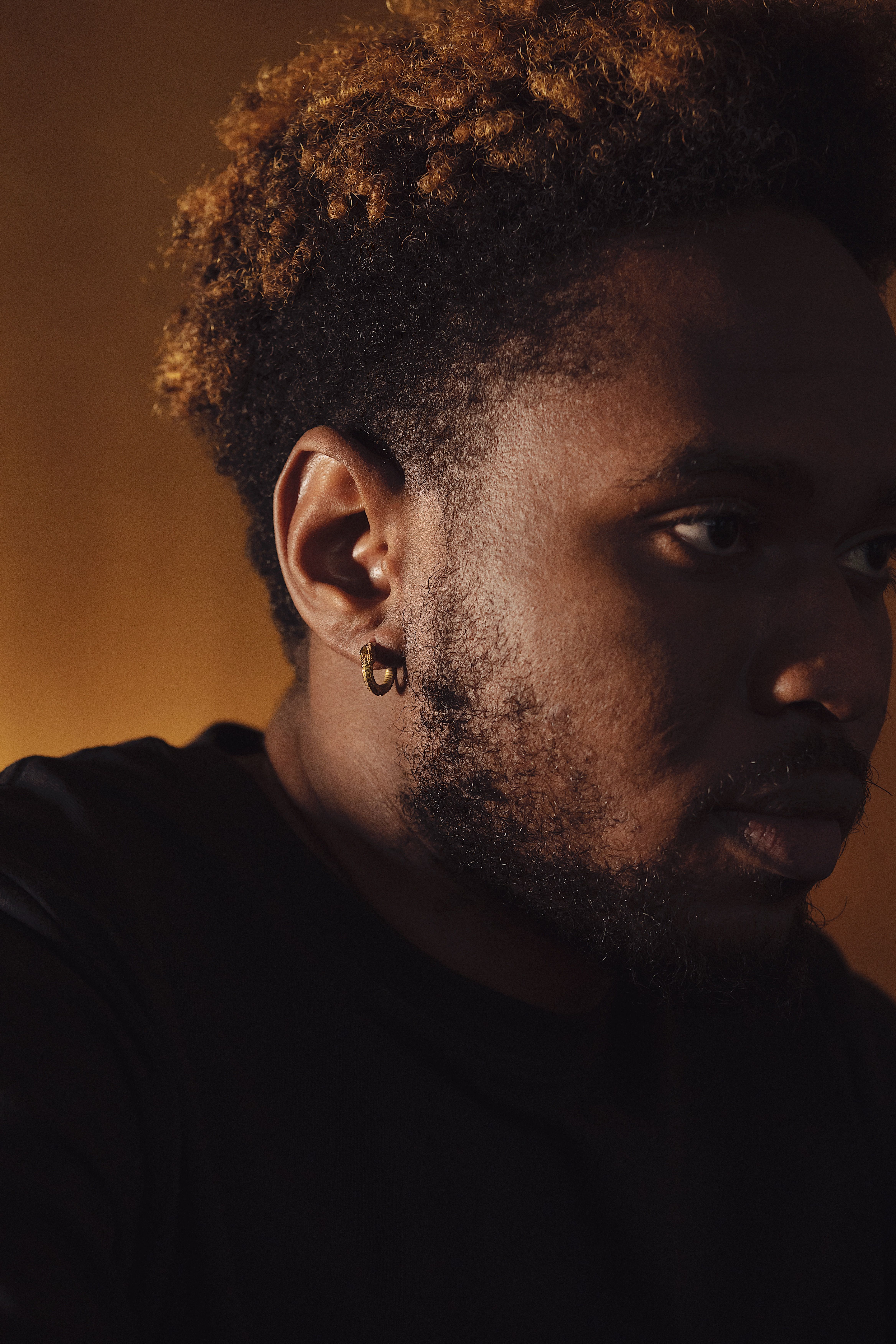 Close-up portrait of a man with a golden earring against a warm backdrop, showing artistic lighting.