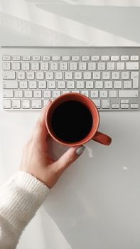 Overhead view of a woman holding a coffee mug over a keyboard, symbolizing a work break.