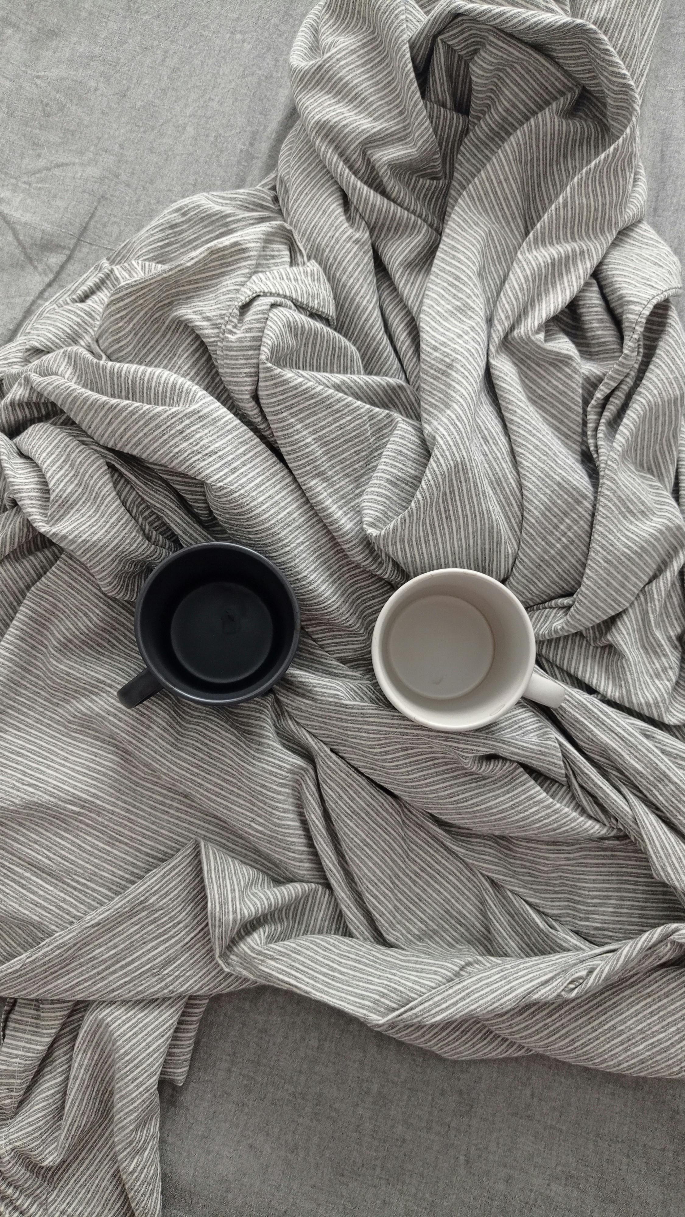 Top view of two coffee mugs on a soft, striped linen background, exuding a minimalist aesthetic.