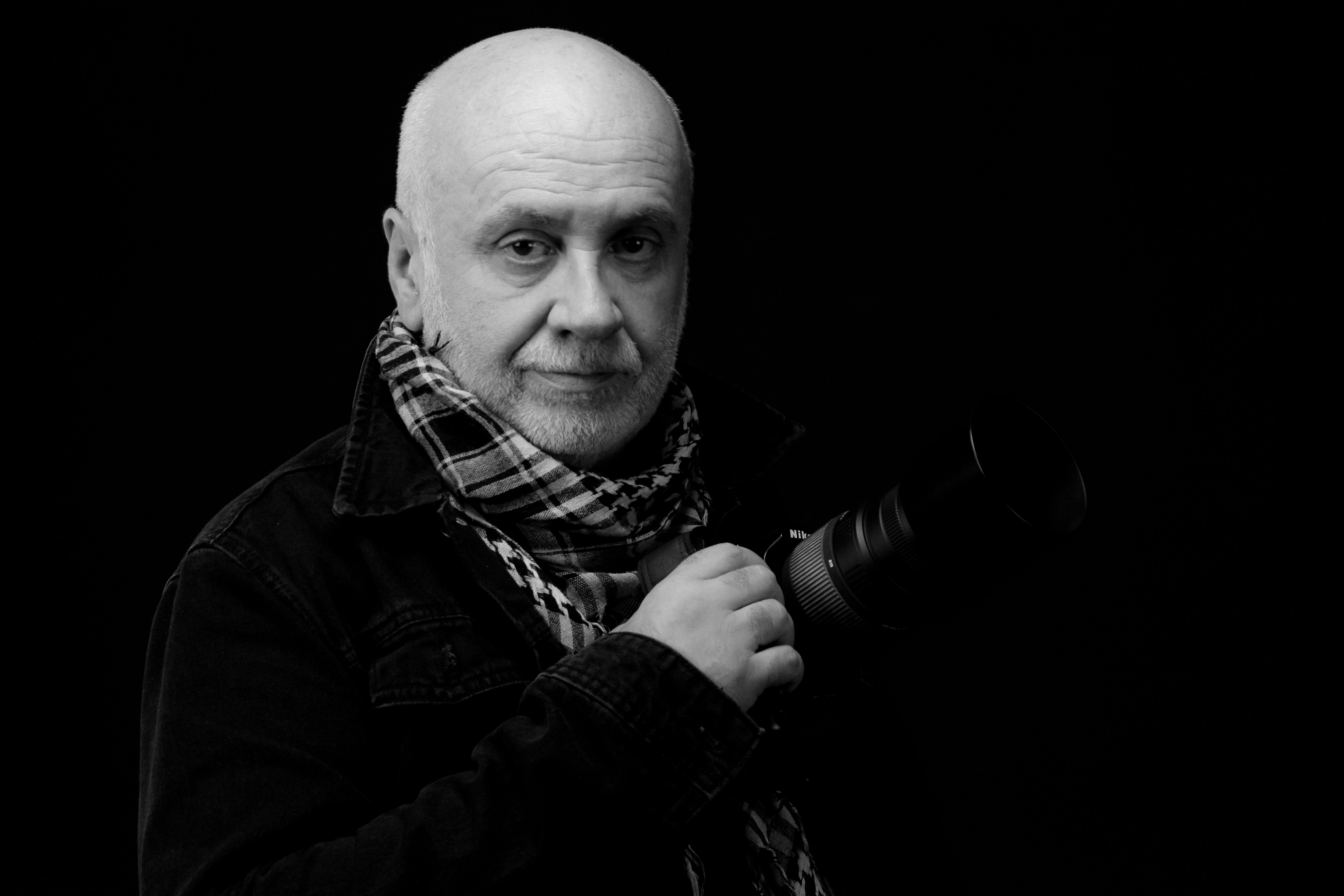 Striking black and white portrait of an elderly photographer holding a camera.