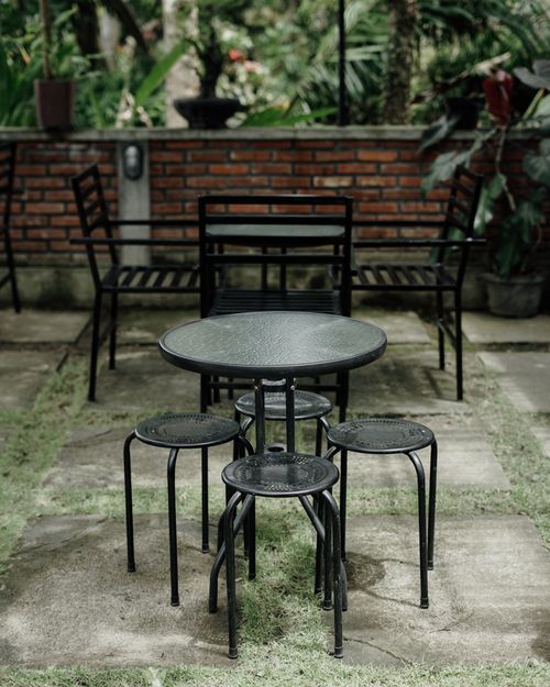 Free Metal table and stools in a lush garden patio setting with brick wall backdrop. Stock Photo