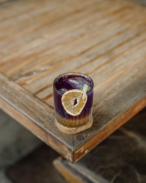 Free A close-up of a vibrant purple beverage with a lemon slice on a wooden table in Denpasar. Stock Photo