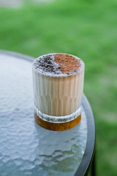 Refreshing iced coffee topped with cocoa and cream on a glass-topped table outdoors.