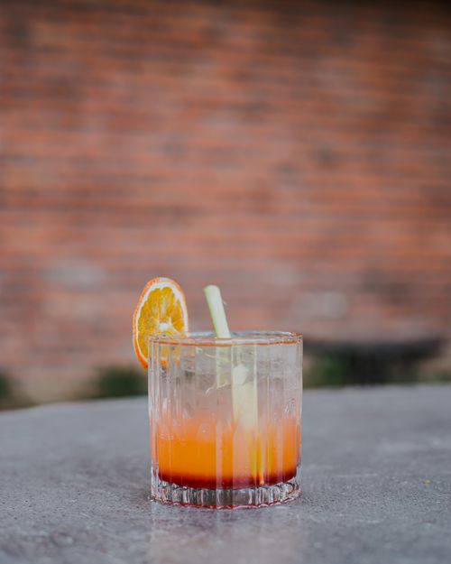 Free Close-up of a vibrant orange cocktail with ice and fresh garnish on a outdoor table. Stock Photo