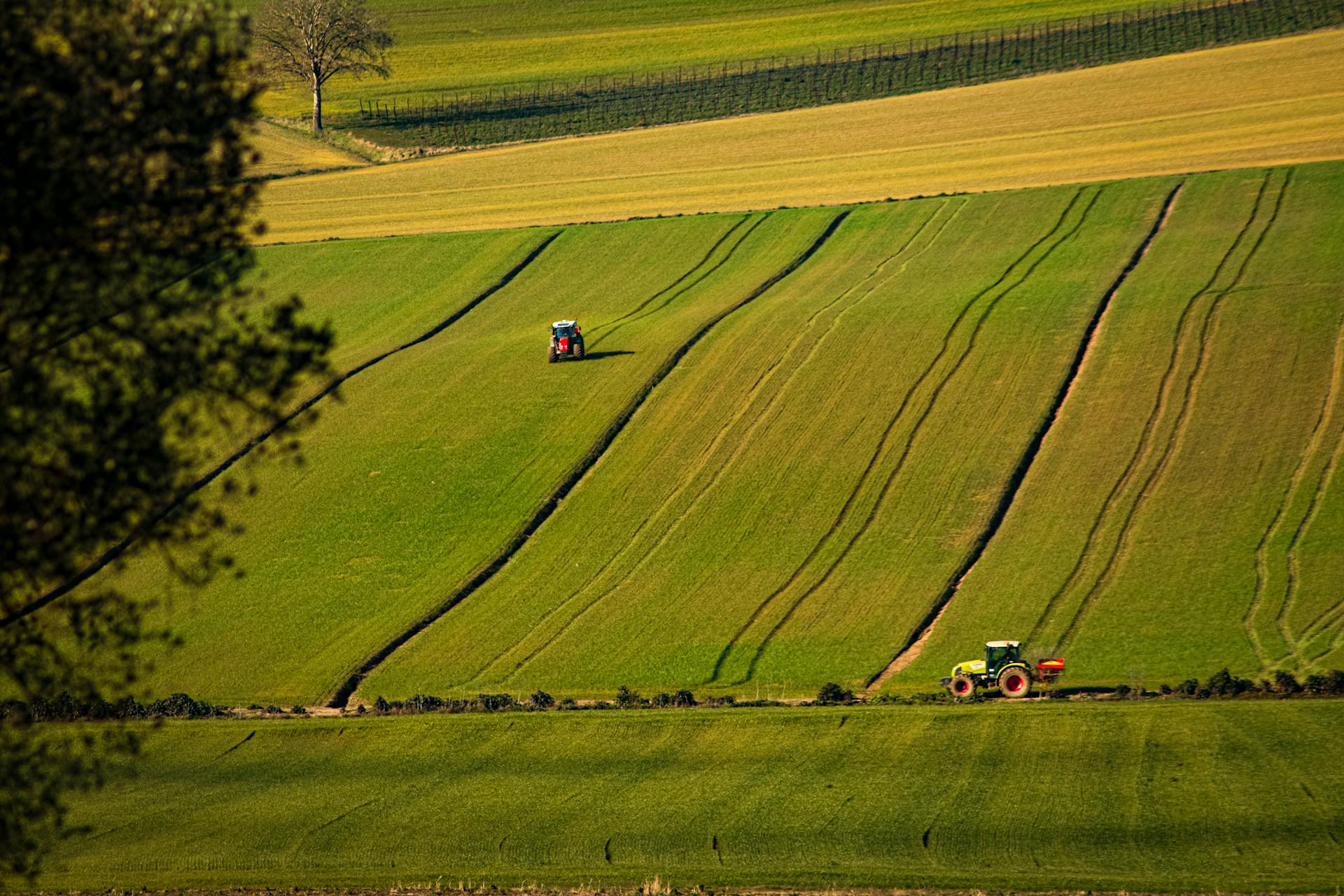 Scenic view of tractors working in green fields of Tuscany, Italy, during spring.