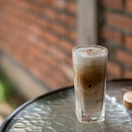 Free Delicious iced coffee with cream and foam served on a glass table indoors. Stock Photo