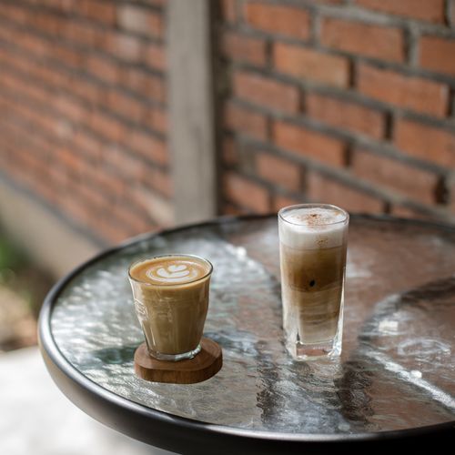 Free Two beautifully crafted coffee drinks on a glass table at an outdoor café. Stock Photo