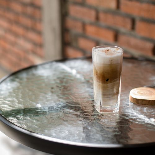 Free Tall iced cappuccino on a glass table with a brick wall background, perfect for summer refreshment. Stock Photo