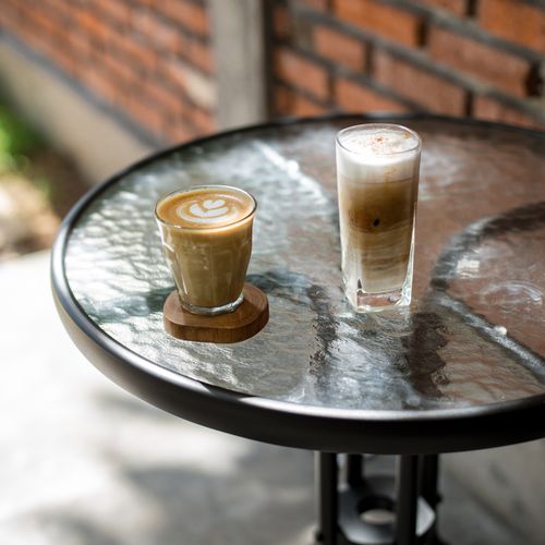 Free An inviting scene of two coffee beverages on a round glass table in a cozy outdoor café setting. Stock Photo