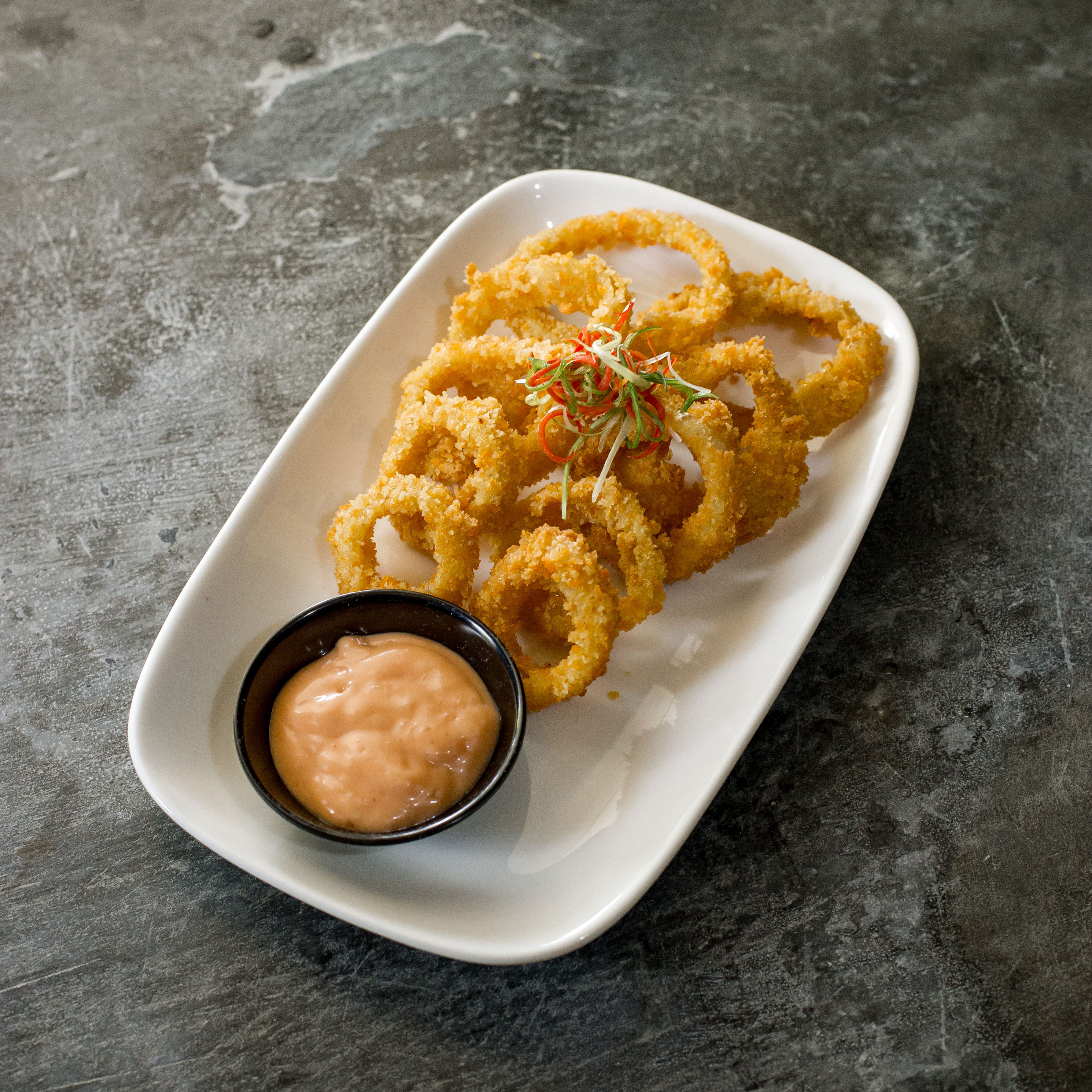 Tasty fried calamari rings served with a tangy dipping sauce on a rustic plate.