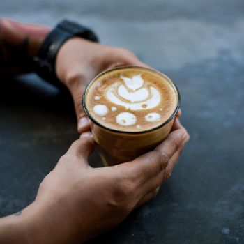 Close-up of a person holding a glass of coffee with intricate latte art.