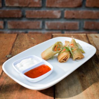 Tasty vegetable spring rolls served with dipping sauces on a rustic wooden table.