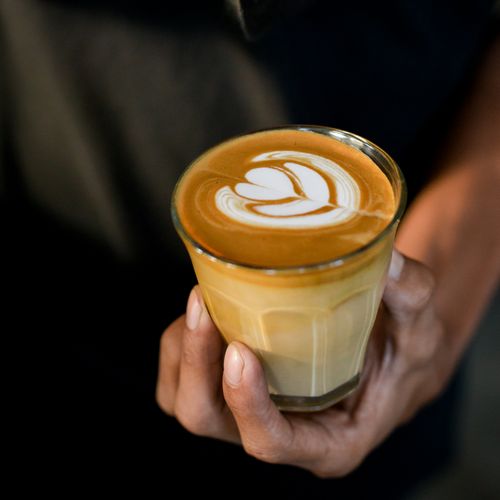 Free A close-up of a hand holding a latte with delicate foam art in a glass. Stock Photo