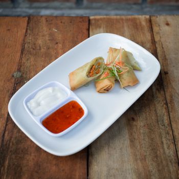 Plate of crispy spring rolls served with tangy dipping sauces on a rustic wooden table.