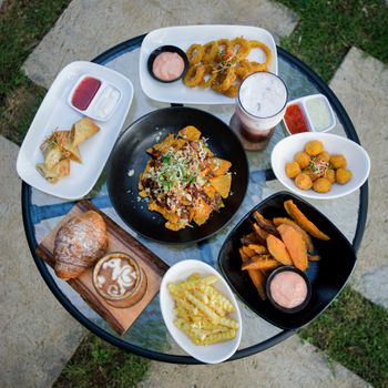 A top-down view of a glass table with various delicious brunch snacks including nachos, croissants, and sweet potato fries.