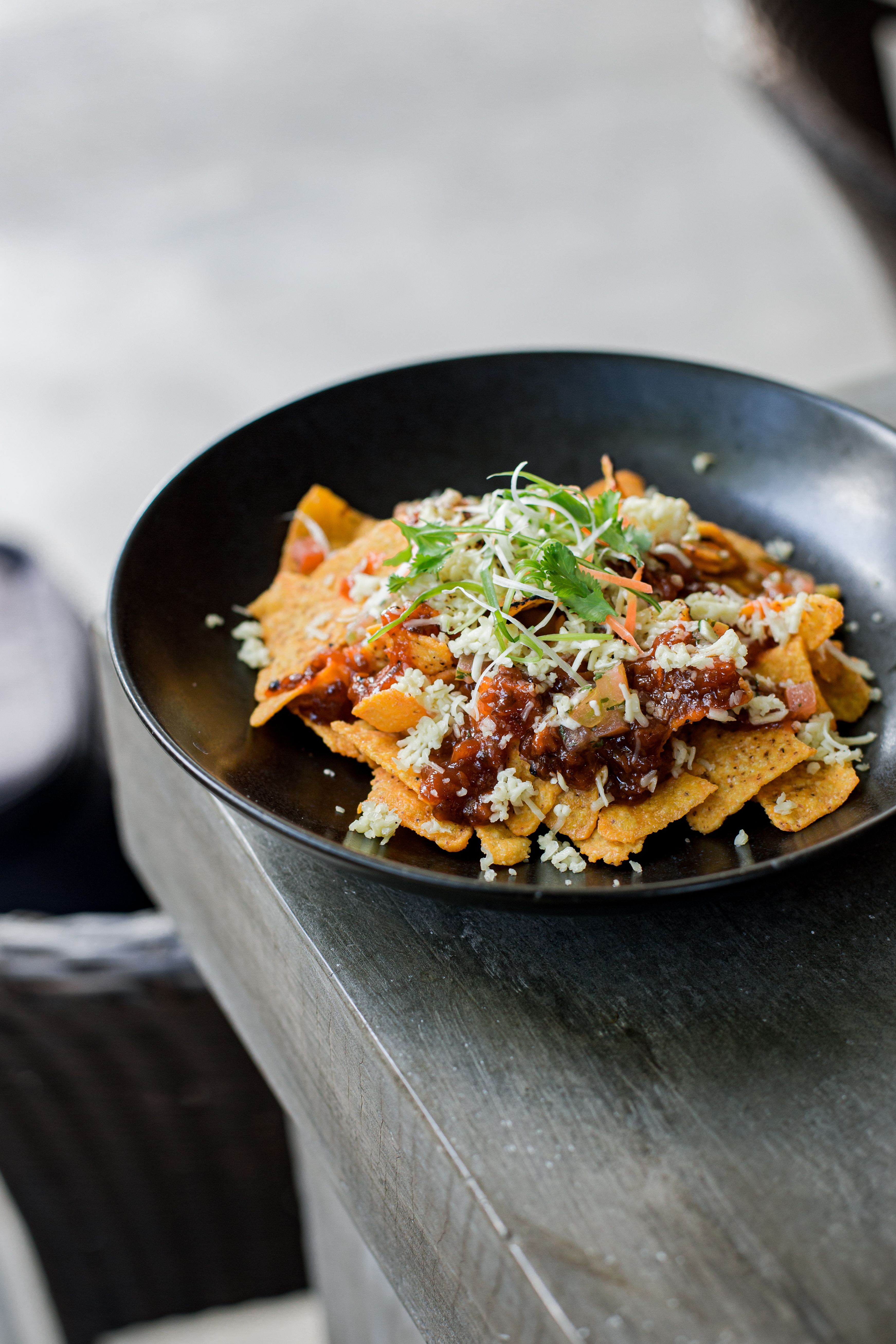 Mouthwatering nachos with toppings served in black plate, ideal for snacks or meals.