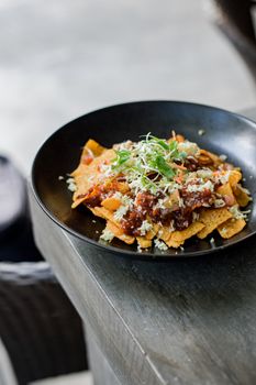 Mouthwatering nachos with toppings served in black plate, ideal for snacks or meals.
