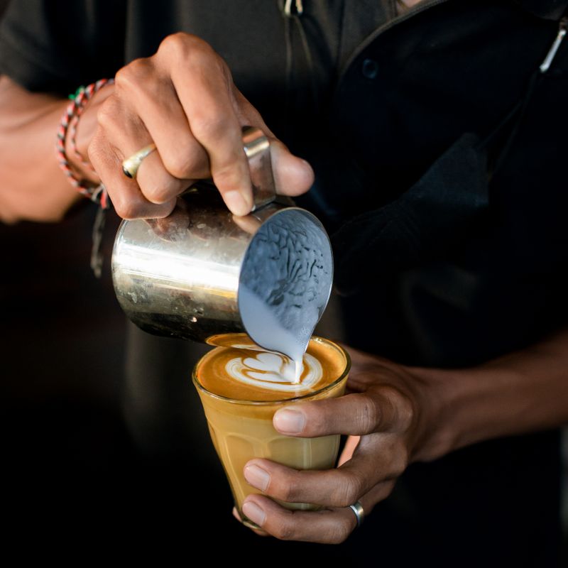 A barista pouring milk into a glass of espresso — photo by Arya Bajra on Pexels