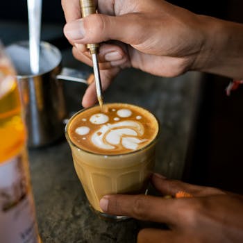Close-up of hands creating intricate latte art on coffee in a café environment.