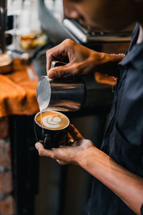 Free Close-up of a barista skillfully pouring latte art into a coffee cup at a cozy cafe. Stock Photo