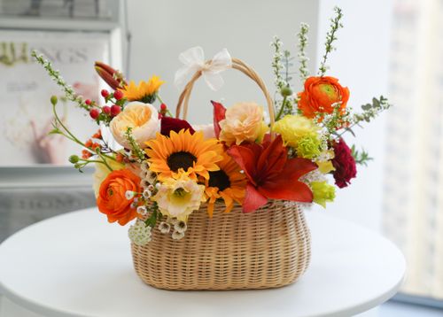 Free A colorful floral arrangement in a straw basket, featuring sunflowers, roses, and lilies. Stock Photo