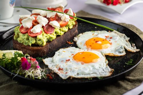 Free Appetizing avocado toast with cherry tomatoes and fried eggs, garnished with herbs. Stock Photo
