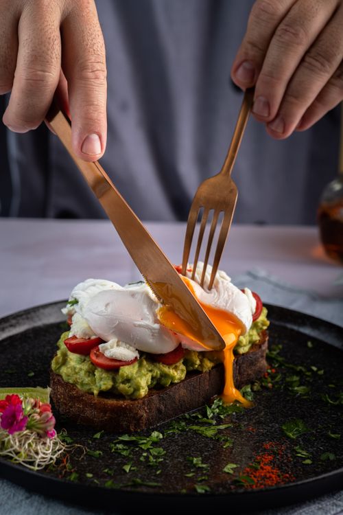 Free Fresh open sandwich with poached egg, avocado, and tomatoes being cut. Stock Photo