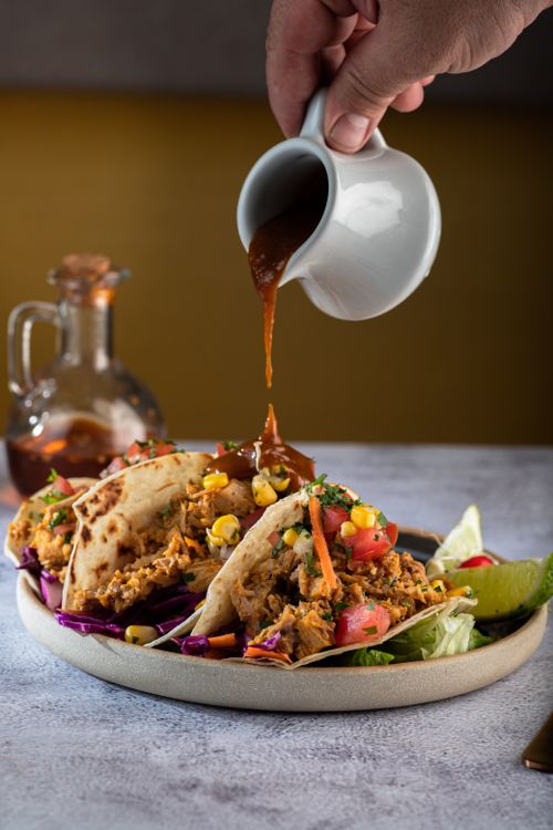 Free Close-up of sauce being poured over tacos with vibrant toppings on a rustic plate. Stock Photo