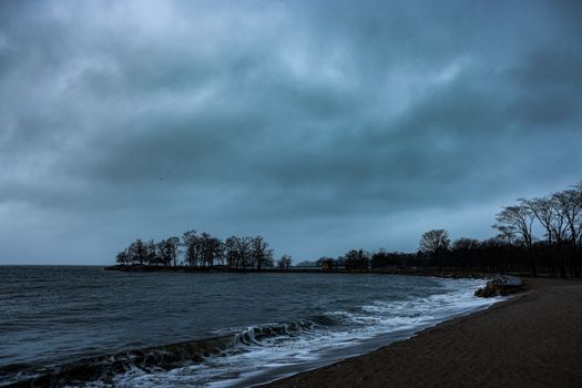 A tranquil coastal beach with dark clouds and waves crashing on the shore.