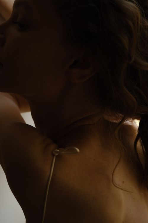 Free A side view close-up of a young woman in soft shadow, captured in a studio with a sensual mood. Stock Photo