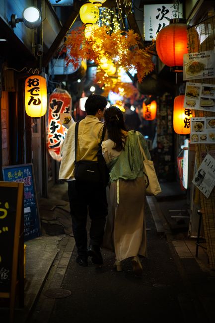 Couple walking through a lantern-lit alley in Tokyo, Japan at night, showcasing urban life.