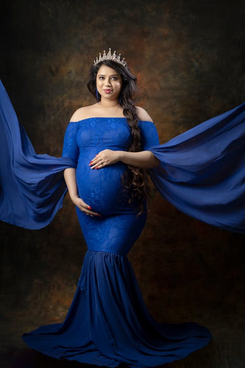 Pregnant Woman in a Blue Dress and a Tiara Posing in Studio 