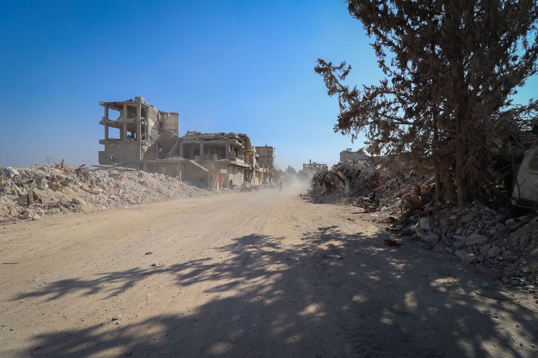 Devastation in Idlib, Syria with destroyed buildings and debris under a clear sky.