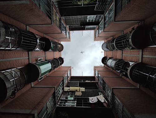 Photo Taken from the Courtyard of an Apartment Building in City with View of an Airplane against a Cloudy Sky