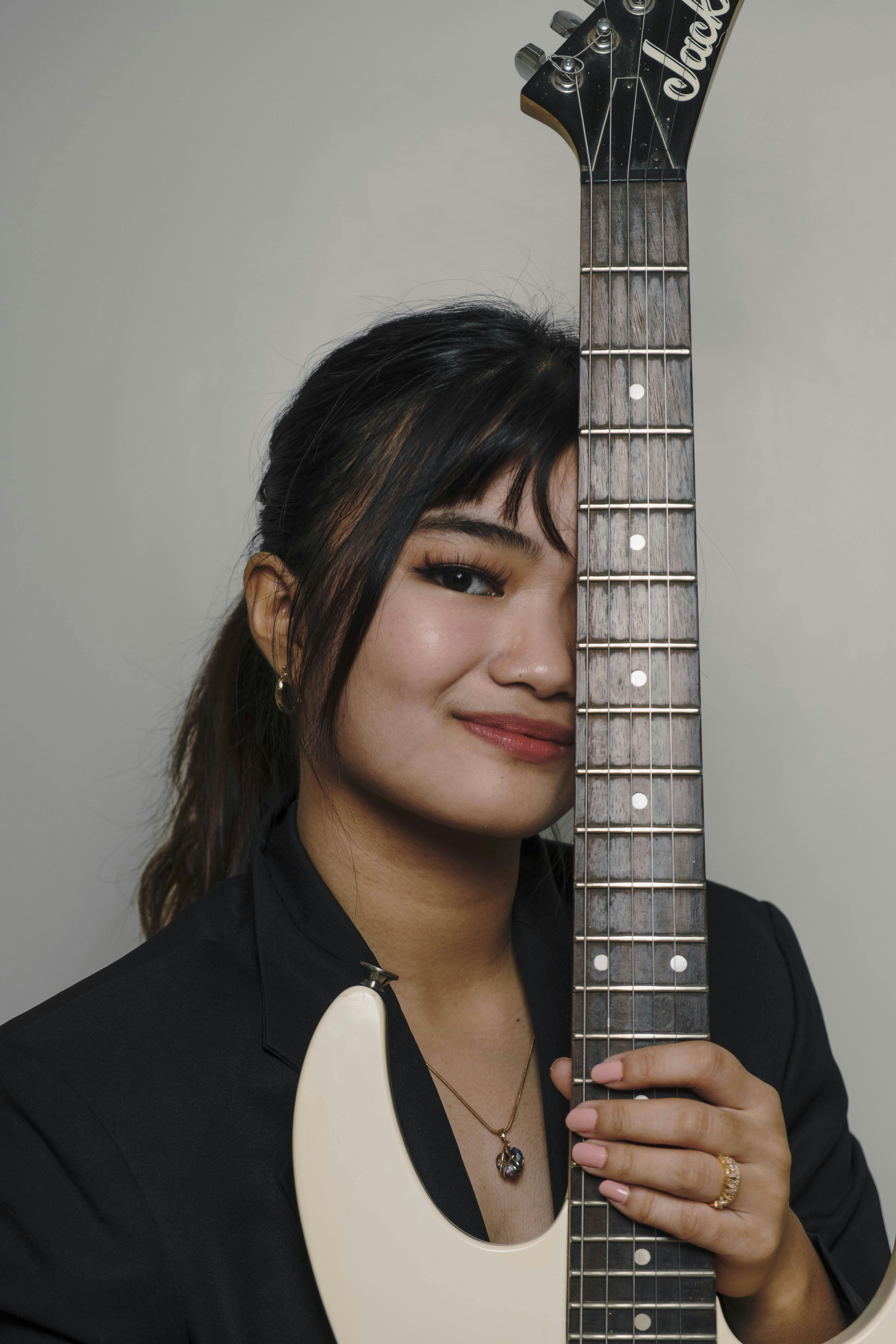 Smiling woman holding an electric guitar against a gray background.