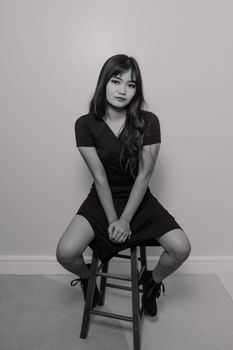 Elegant black and white portrait of a woman sitting on a stool, exuding classic fashion sense.