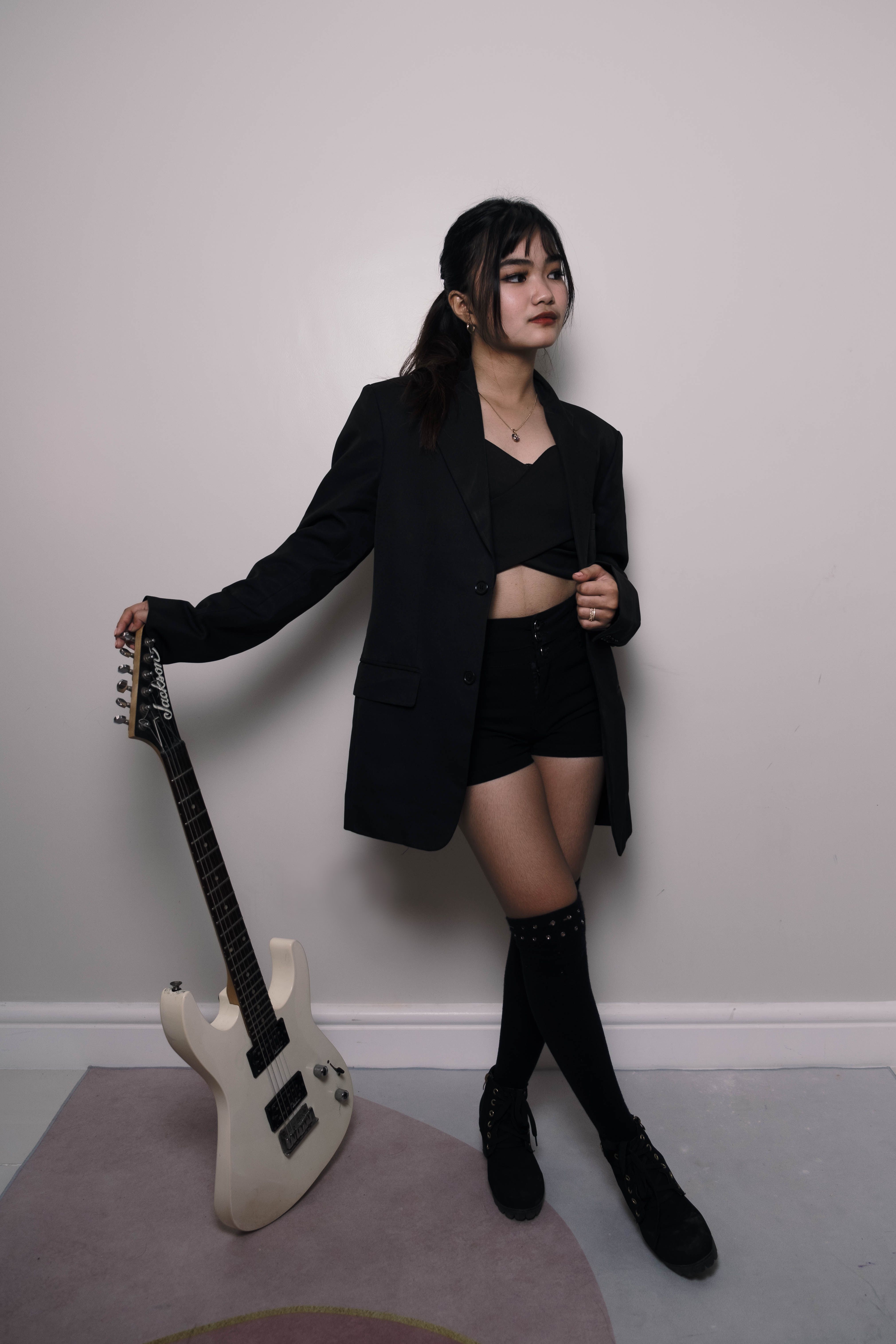 Young woman in a chic outfit posing with an electric guitar indoors.