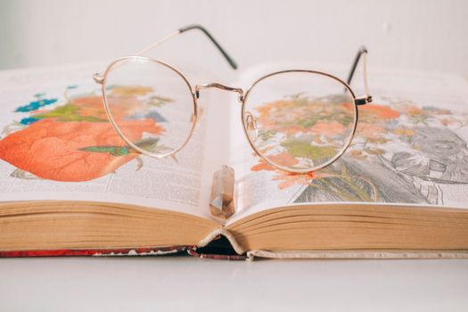 A pair of eyeglasses resting on an open book filled with colorful illustrations and drawings.