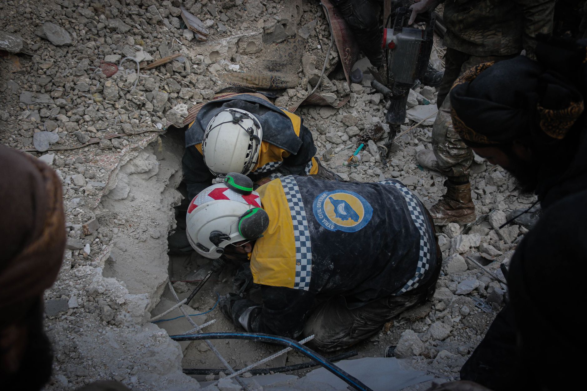 Rescue workers from civil defense searching rubble for survivors in Idlib, Syria, post-disaster.