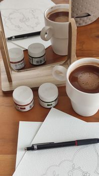 A cozy workspace featuring a cup of coffee, art supplies, and a mirror reflection, perfect for creative projects.