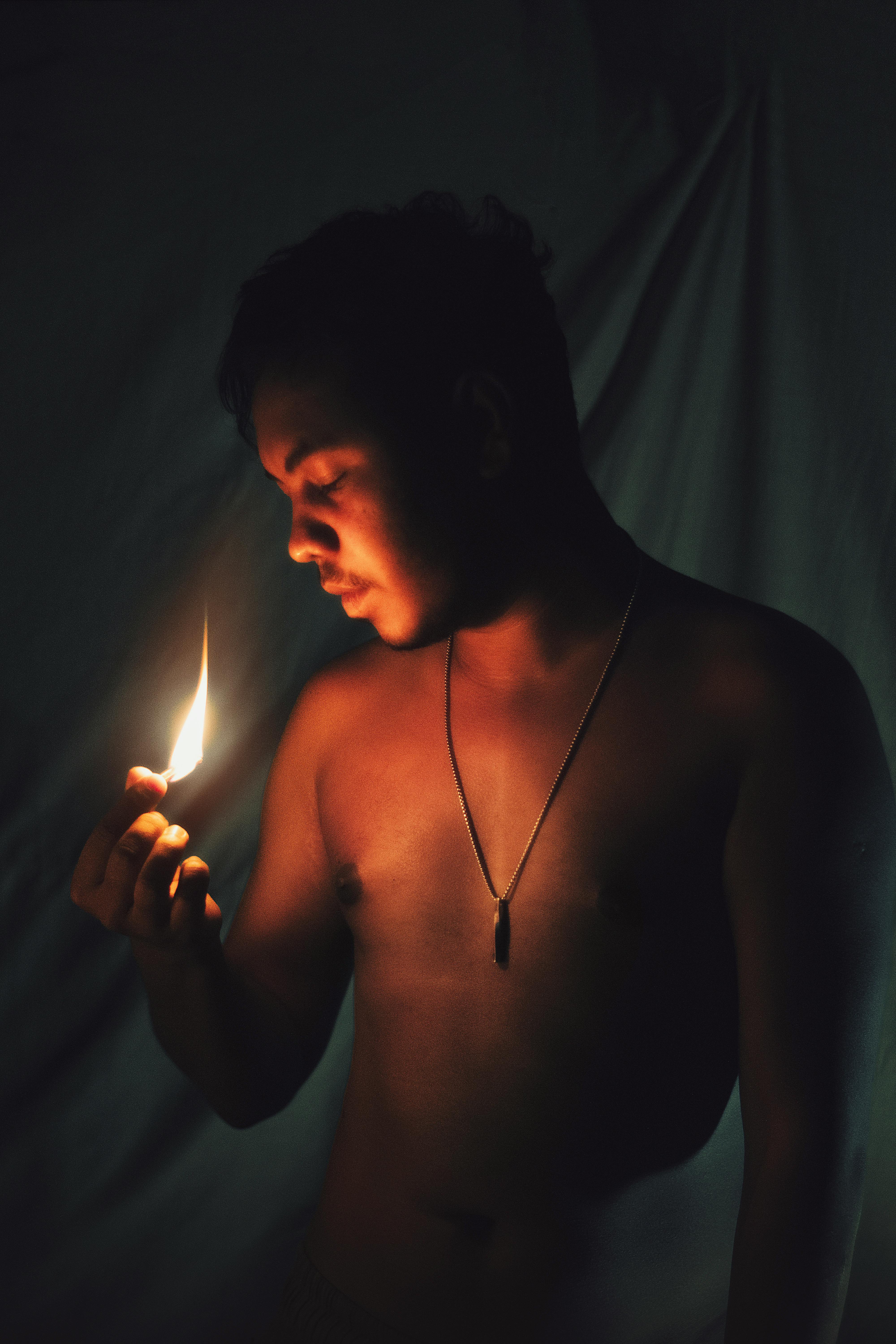 Intimate portrait of a young shirtless man holding a flame, creating a dramatic shadow effect.