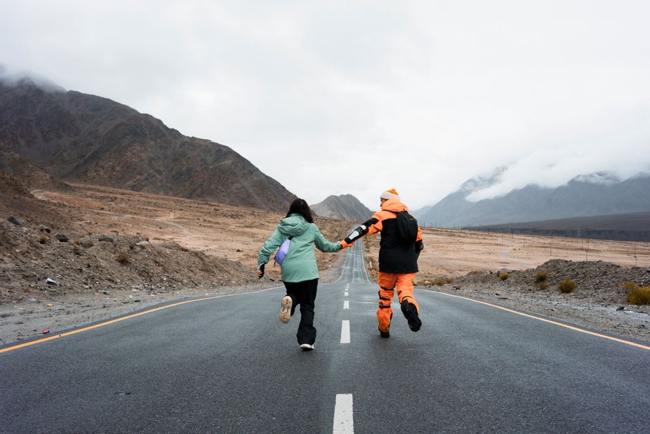 A couple joyfully runs down a scenic mountain road in Ladakheda, MP, India, surrounded by misty peaks.