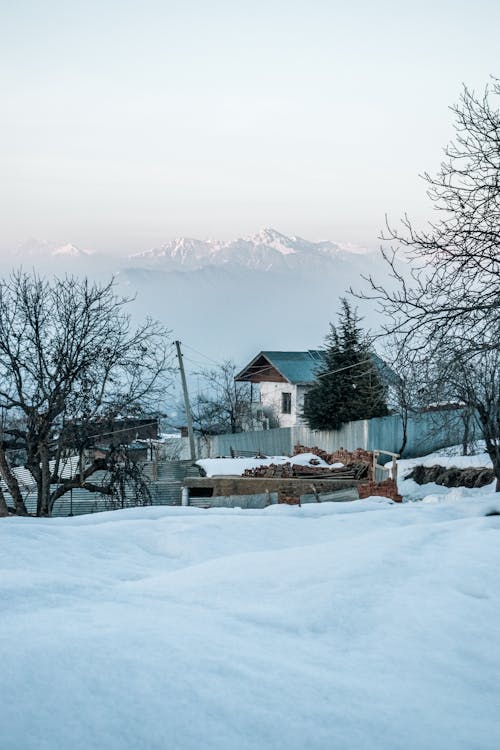 View of a House in a Village Covered in Snow and Mountains in the Background 