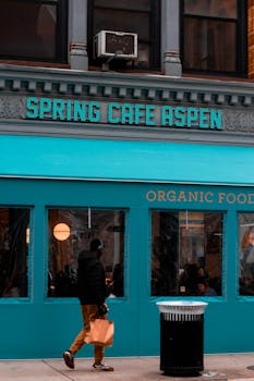 A person walks by Spring Cafe Aspen in New York City, featuring vibrant teal facade.