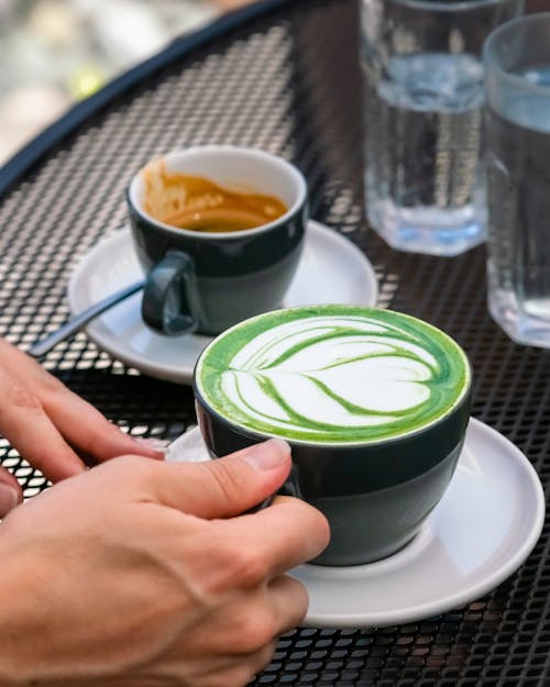 Close-up of Person Holding a Cup with Matcha on a Table in a Cafe