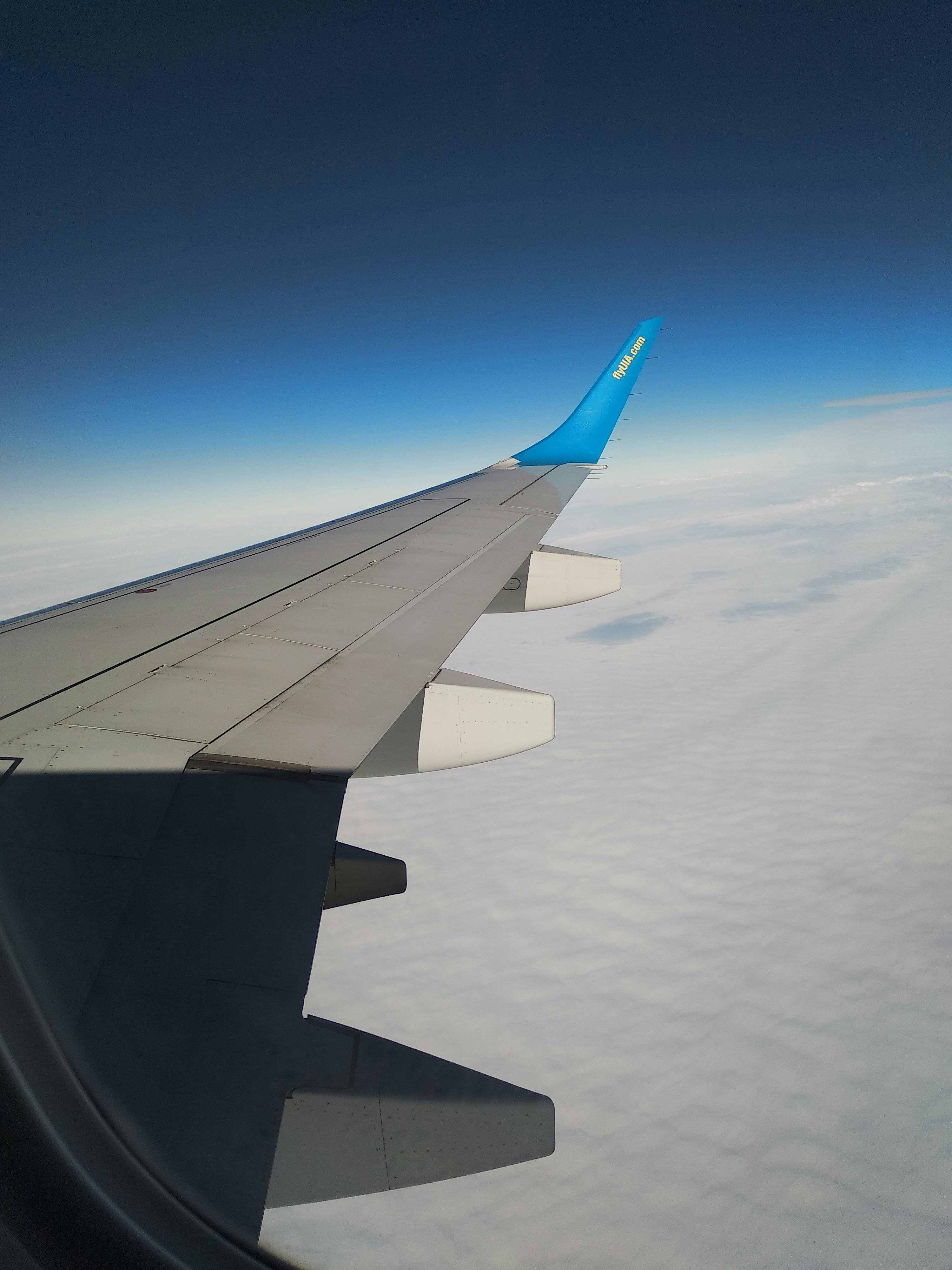 A scenic view of an airplane wing above white clouds and blue sky from a flight.